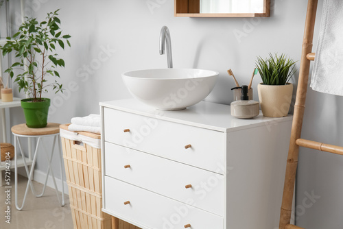 Chest of drawers with sink  toothbrushes  soap and houseplant in light bathroom