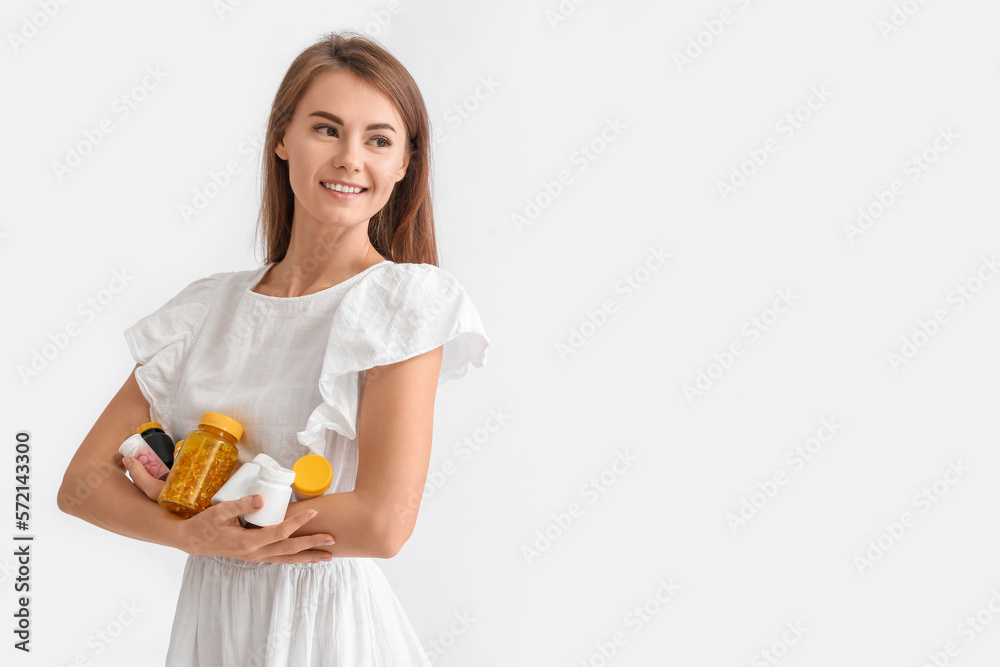Beautiful woman with bottles of vitamin supplements on grey background Beautiful woman with bottles of vitamin supplements on grey background
