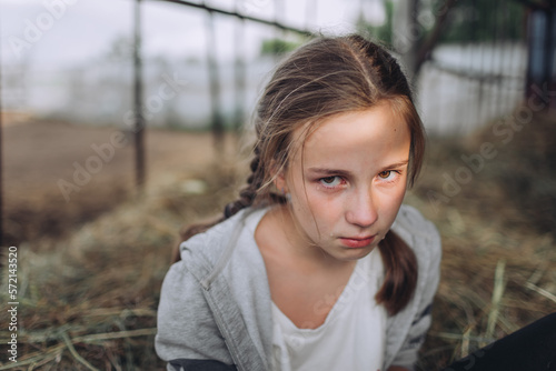 Sad teenage girl looking at camera, tears on face, depressed young girl sitting outdoors on hay
