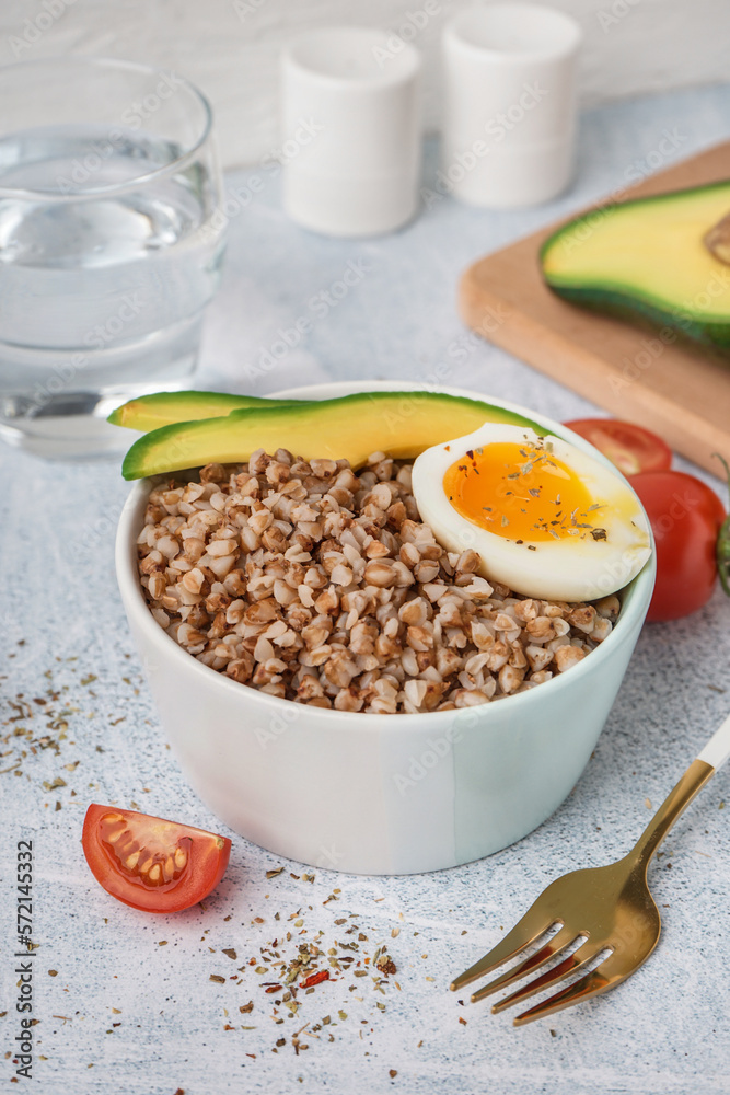 Bowl of tasty buckwheat porridge with soft boiled egg and fresh vegetables on grey table Bowl of tasty buckwheat porridge with soft boiled egg and fresh vegetables on grey table