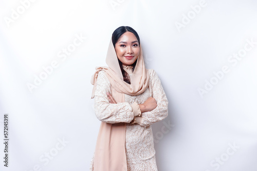 Portrait of a confident smiling Asian Muslim woman wearing hijab standing with arms folded and looking at the camera isolated over white background