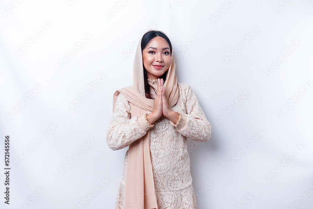 Naklejka premium Portrait of a young beautiful Asian Muslim woman wearing a hijab gesturing Eid Mubarak greeting