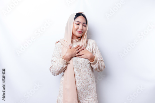 Happy mindful thankful young Asian Muslim woman with her hand on her chest smiling isolated on white background