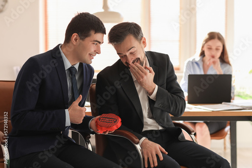 Young men with whoopee cushion laughing in office. April Fools' Day celebration photo
