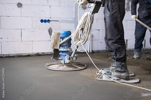 Ramming and grinding of semi-dry floor screed by a machine with a rotating disk for leveling. Construction of a concrete floor in the house, a master with special equipment. photo