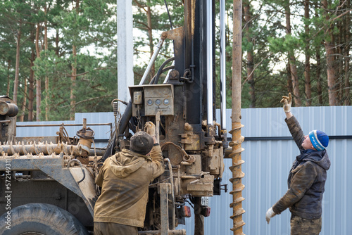 Team of workers with drilling rig on car are drilling artesian well for water in ground. Insertion of metal casing pipe into ground, installation of individual drinking supply, June 28, 2022, Russia, photo