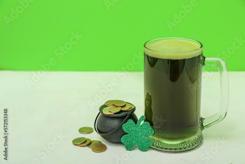 Glass of beer, pot with coins and paper clover on table near green wall. St. Patrick's Day celebration