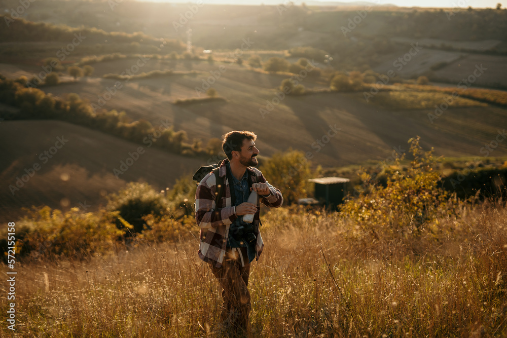 Side view of a cheerful hiker, walking up the hill and about to drink water, enjoying the view. Side view of a cheerful hiker, walking up the hill and about to drink water, enjoying the view.