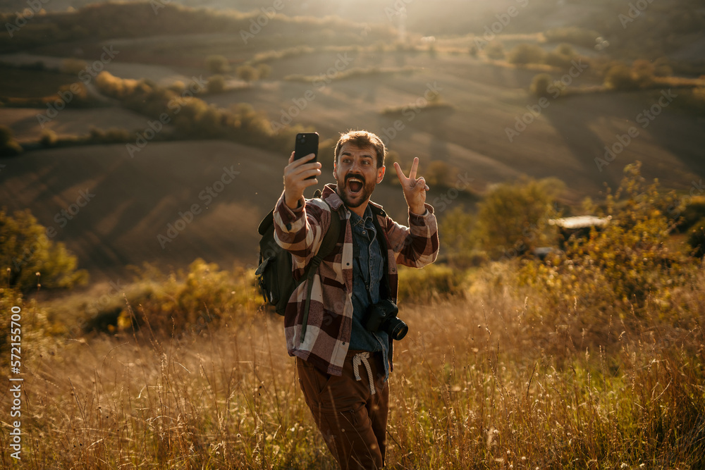 A young hiker man standing on the mountain peak, having a video call and showing the landscape A young hiker man standing on the mountain peak, having a video call and showing the landscape