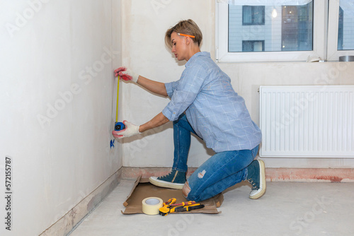 Repair work of home. Woman with tape measure measuring walls. Renovation in new apartment. High quality photo