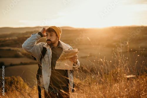Fotografie Shot of a young lost hiker holding a map while exploring golden hill fields