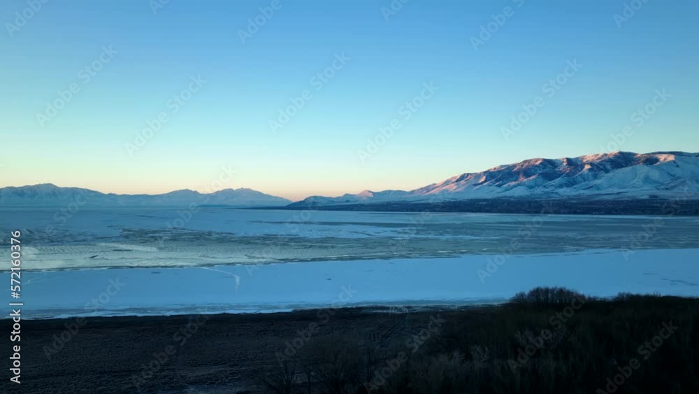 A huge frozen lake below a snowy mountain at dawn - aerial A huge frozen lake below a snowy mountain at dawn - aerial