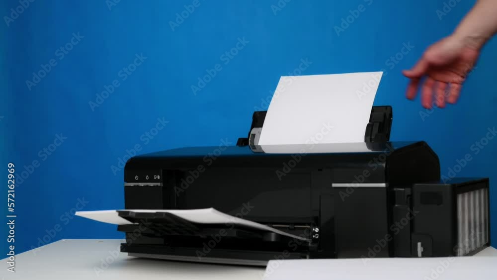 Paper Into Printer A hand inserts blank sheets of A4 paper into the printer on a blue ...