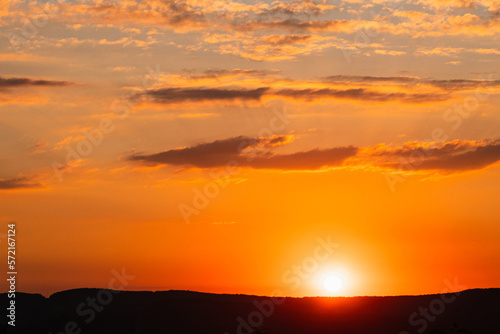 Summer sunset with yellow and orange colours. Beautiful clouds in the sky. The sun hovers over the mountain. The sun's rays from below illuminate the dark clouds. The beauty of nature.