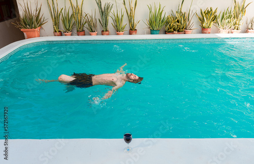 Man on vacation swimming on his back in a swimming pool. Young man swimming on his back in a hotel pool. Concept of man on vacation enjoying the pool