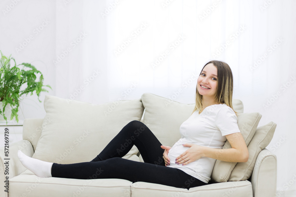 Smiling pregnant woman sitting on white sofa.
