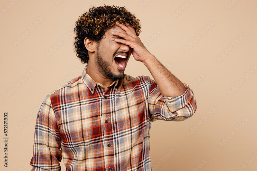 Sad upset Indian man wear brown shirt casual clothes put hand on face facepalm epic fail mistaken omg gesture isolated on plain pastel light beige background studio portrait. People lifestyle concept. Sad upset Indian man wear brown shirt casual clothes put hand on face facepalm epic fail mistaken omg gesture isolated on plain pastel light beige background studio portrait. People lifestyle concept.