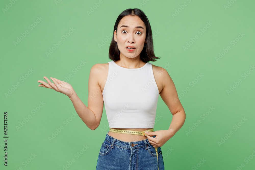 Φωτογραφία Young sad confused woman wears white tank shirt hold measuring tape on waist spread hand isolated on plain pastel light green background