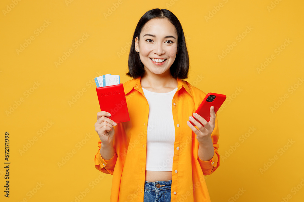 Young woman wear summer clothes hold passport ticket use mobile cell phone isolated on plain yellow background. Tourist travel abroad in free spare time rest getaway. Air flight trip journey concept. Young woman wear summer clothes hold passport ticket use mobile cell phone isolated on plain yellow background. Tourist travel abroad in free spare time rest getaway. Air flight trip journey concept.