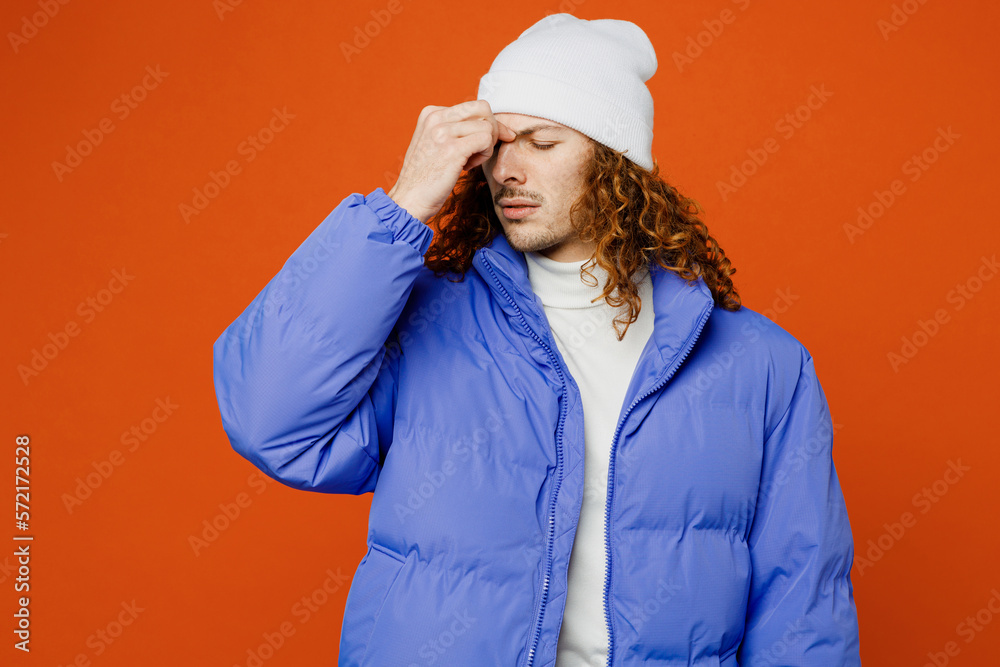 Young dissatisfied upset shocked man with long curly hair wear hat purple ski padded jacket casual clothes keep eye closed rub put hand on nose isolated on plain orange red background studio portrait Young dissatisfied upset shocked man with long curly hair wear hat purple ski padded jacket casual clothes keep eye closed rub put hand on nose isolated on plain orange red background studio portrait