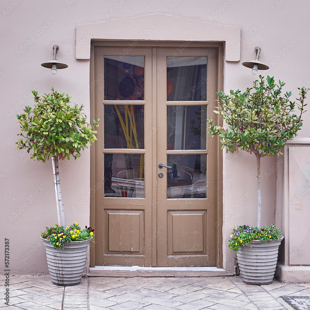 Vintage double pale brown painted door and potted laurel plants by the sidewalk. Travel to Athens, Greece.
