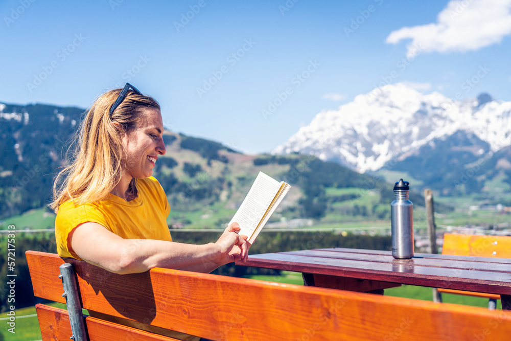 Young beautiful and happy girl reading a book on a bench, mounta Young beautiful and happy girl reading a book on a bench, mounta