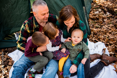 Smiling family looks at baby sitting on  blanket in Fall leaves campin photo
