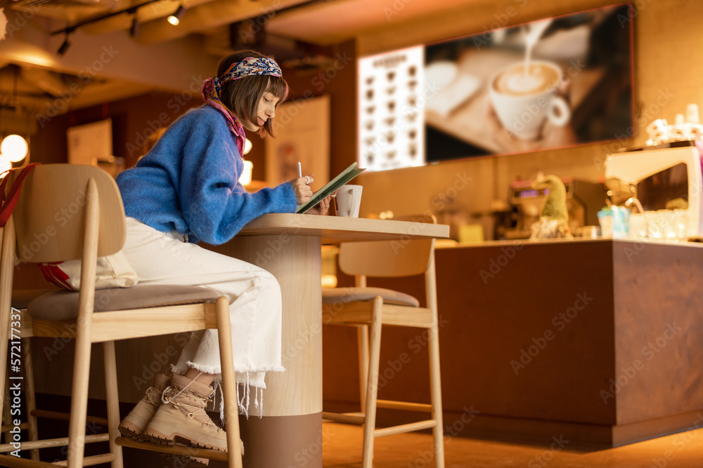 Young adult woman works on a digital tablet while sitting at modern coffee shop. Concept of remote creative work online