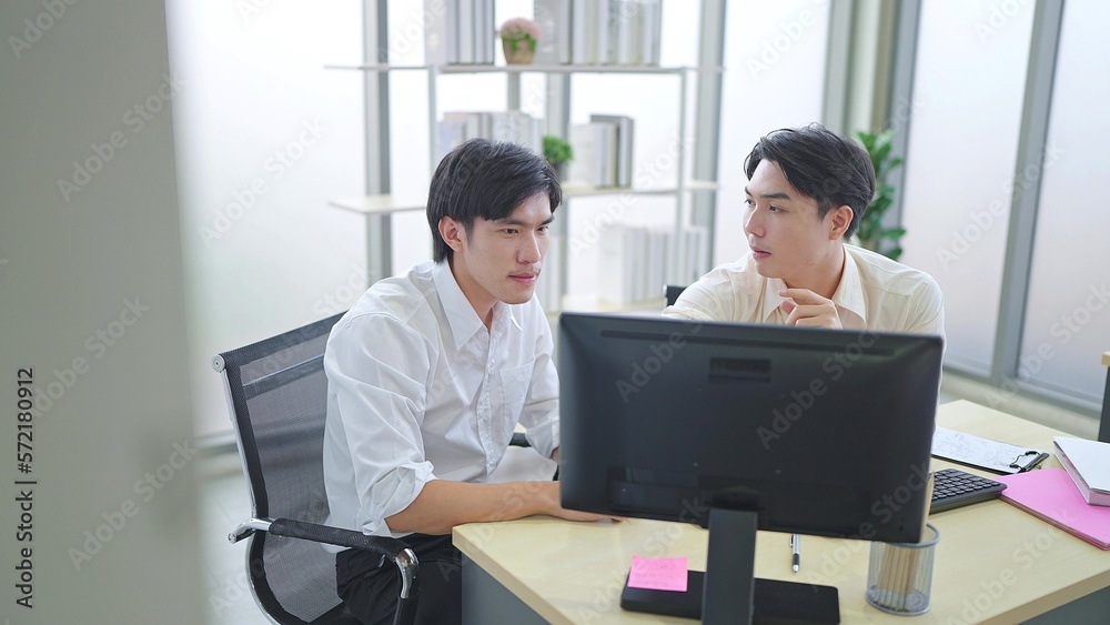 Two young asian businessmen discussing financial market data and using computer on desk at office Two young asian businessmen discussing financial market data and using computer on desk at office