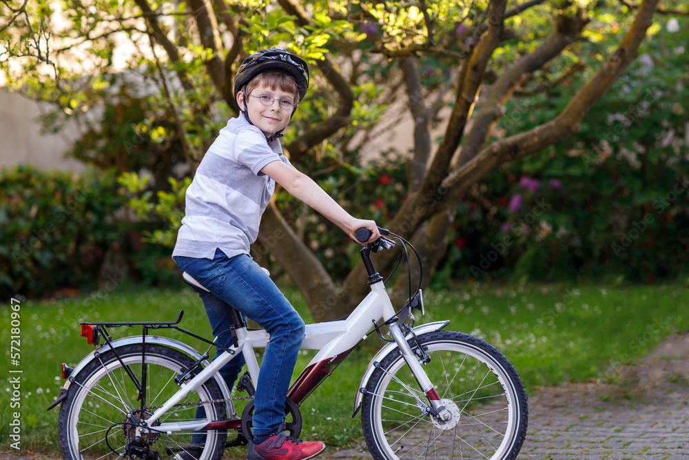 Fototapeta premium Happy school kid boy having fun with riding of bicycle. Active child with safety helmet making sports with bike in nature. Safety, sports, leisure with kids concept