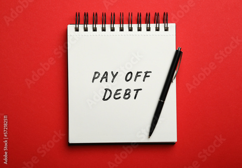 Notebook with phrase Pay Off Debt and pen on red background, top view © New Africa