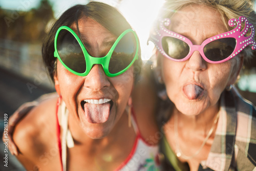 Funny, selfie and tongue out by senior women with sunglasses outdoors for travel, break and bonding on blurred background. Emoji, face and crazy elderly friends pose for photo, profile picture or fun