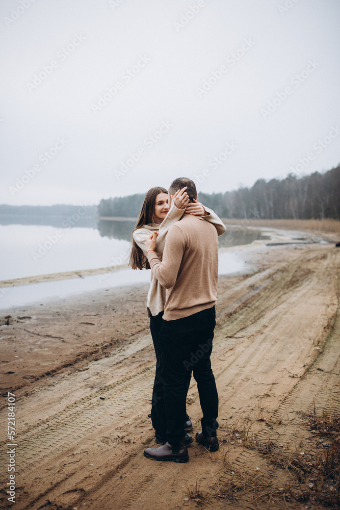 a love story of a man and a woman hugging on the shore of a foggy lake. stylish couple in beige sweaters in cold weather on the lake. happy people in love. love warms in cold weather a love story of a man and a woman hugging on the shore of a foggy lake. stylish couple in beige sweaters in cold weather on the lake. happy people in love. love warms in cold weather