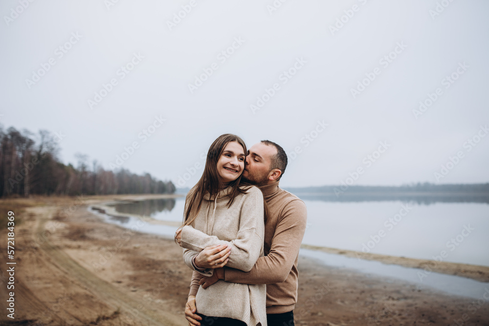 a love story of a man and a woman hugging on the shore of a foggy lake. stylish couple in beige sweaters in cold weather on the lake. happy people in love. love warms in cold weather