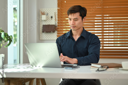 Handsome businessman using laptop computer working at home office. Remote job, technology and lifestyle concept