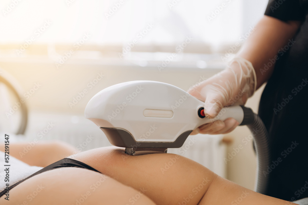 Fototapeta premium Body Care. Legs Laser Hair Removal. Beautician Removing Hair Of Young Woman's Leg. Laser Epilation Treatment In Cosmetic Beauty Clinic. Hairless Smooth And Soft Skin. Health And Beauty Concept.