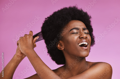 Stress, hairstyle and afro brushing on beauty studio background in grooming, texture anxiety or crisis. Black woman, comb and natural hair with damage, split ends or frizzy knots on isolated skincare