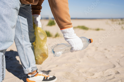 Young man collecting in plastic bag rubish and plastic bottles on the beach photo