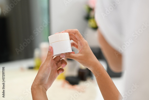 Over shoulder view of woman holding jar with moisturizing cream. Home care, Beauty treatment concept