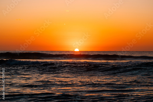 Sunrise from ocean horizon with clear sky.