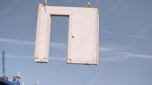 Concrete building panel with door frame moved by construction crane.