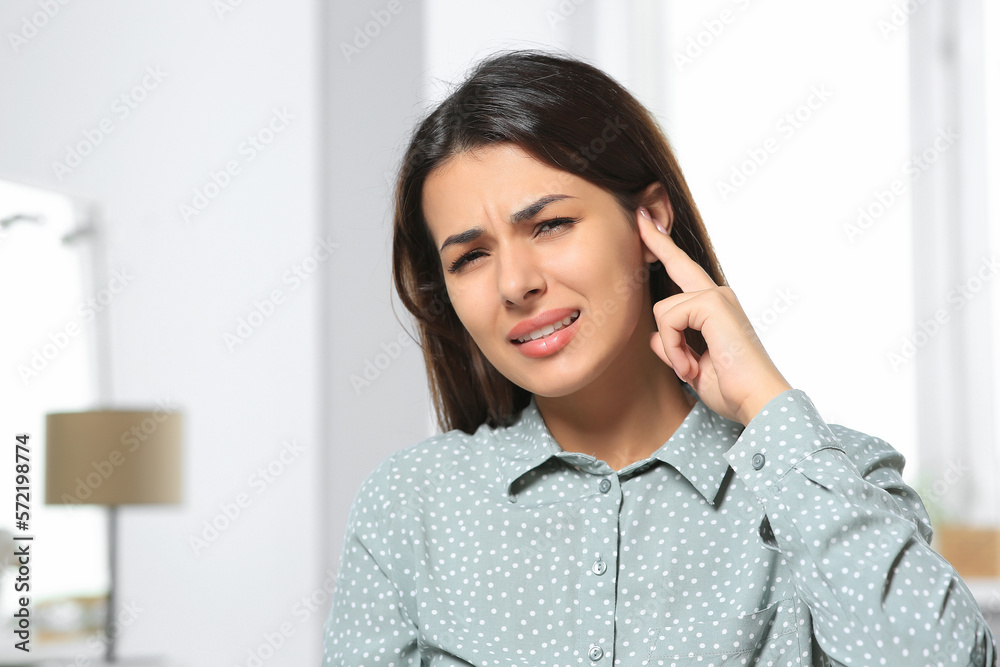 Young woman suffering from ear pain indoors