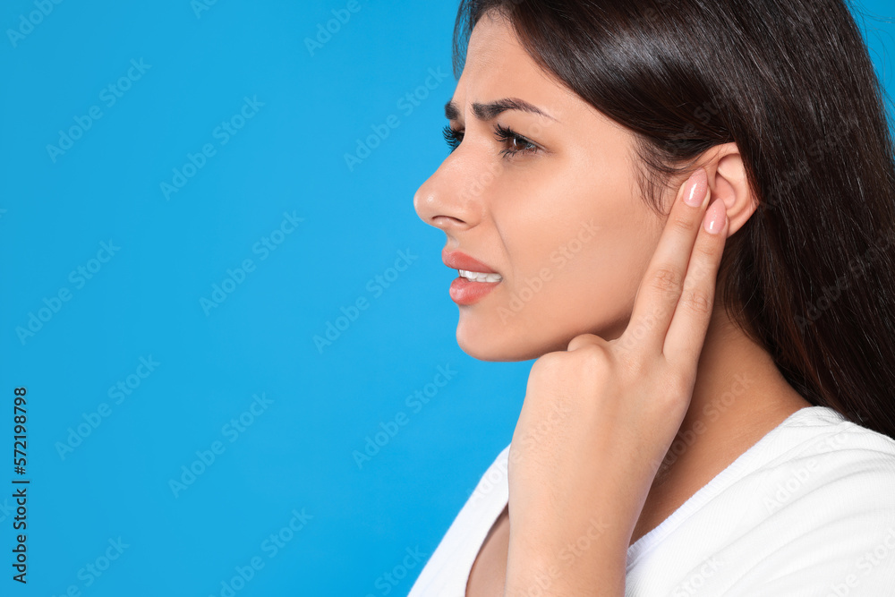 Young woman suffering from ear pain on light blue background, closeup. Space for text Young woman suffering from ear pain on light blue background, closeup. Space for text