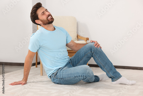 Man touching knee on white carpet near armchair at home