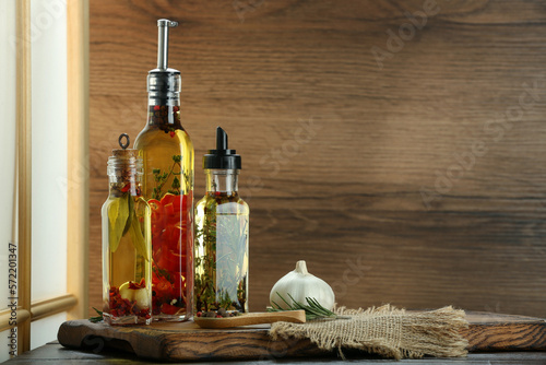 Cooking oil with different spices and herbs in bottles on wooden table. Space for text