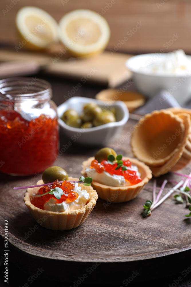Delicious tartlets with red caviar and cream cheese served on wooden board, closeup Delicious tartlets with red caviar and cream cheese served on wooden board, closeup