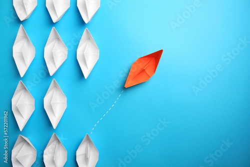 Orange paper boat floating away from others on light blue background, flat lay with space for text. Uniqueness concept