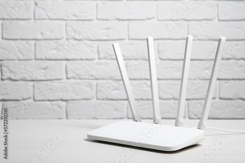 New Wi-Fi router on white wooden table against brick wall. Space for text