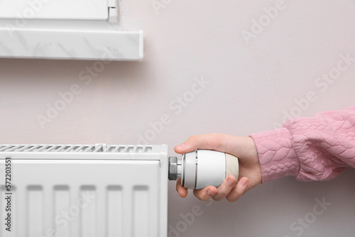 Girl adjusting heating radiator thermostat near white wall indoors, closeup