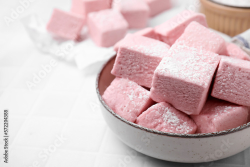 Bowl of delicious sweet marshmallows with powdered sugar on white table, closeup. Space for text